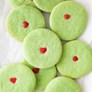 closeup of round green grinch sugar cookies with a red heart on each