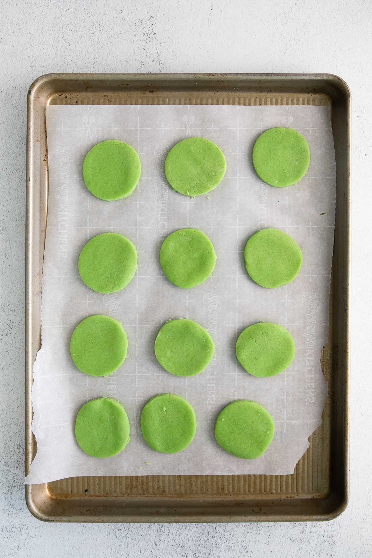 twelve green round uncooked cookies on a parchment lined baking sheet