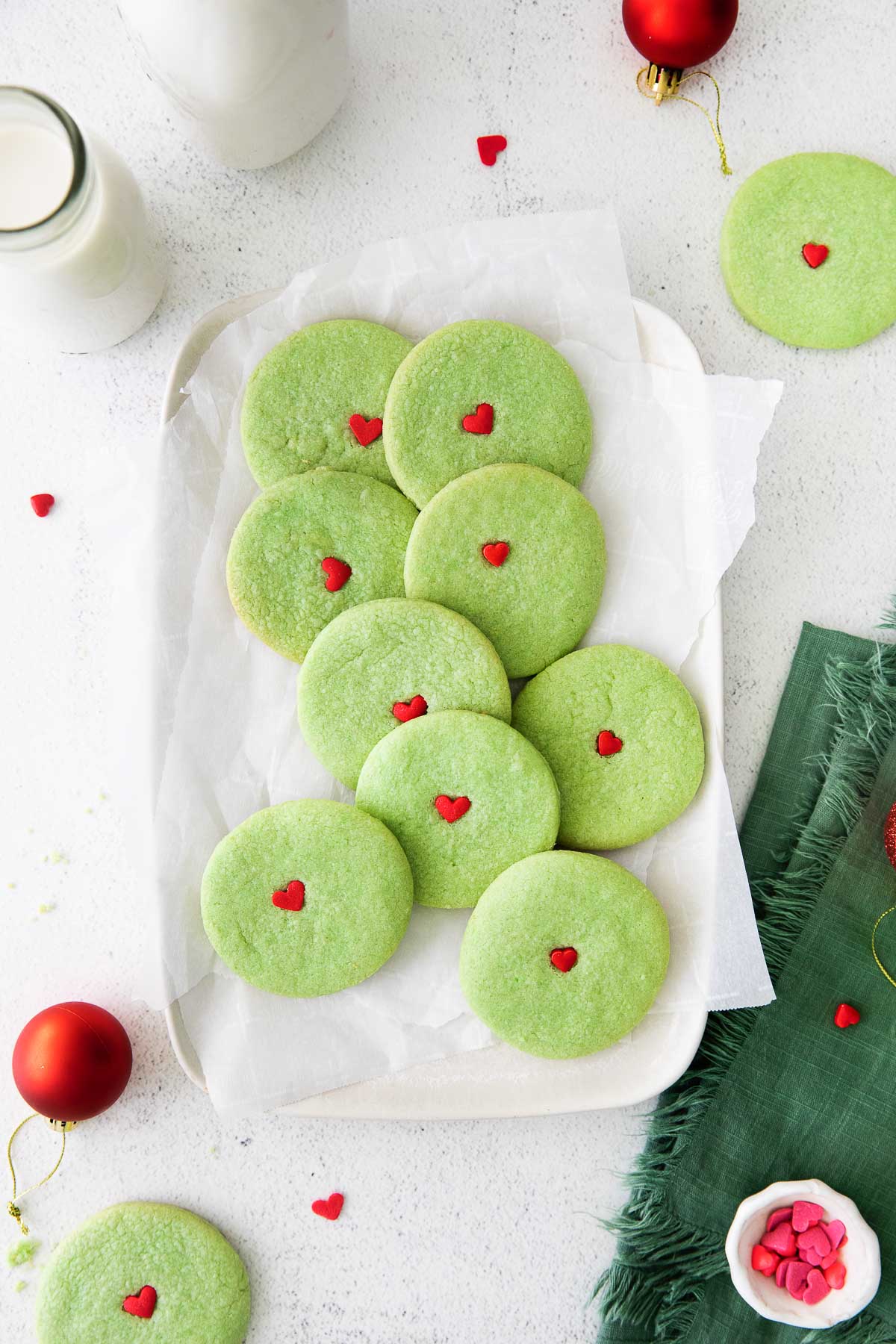 white rectangle plate with a with several round green sugar cookies with a red heart in the center of each cookies