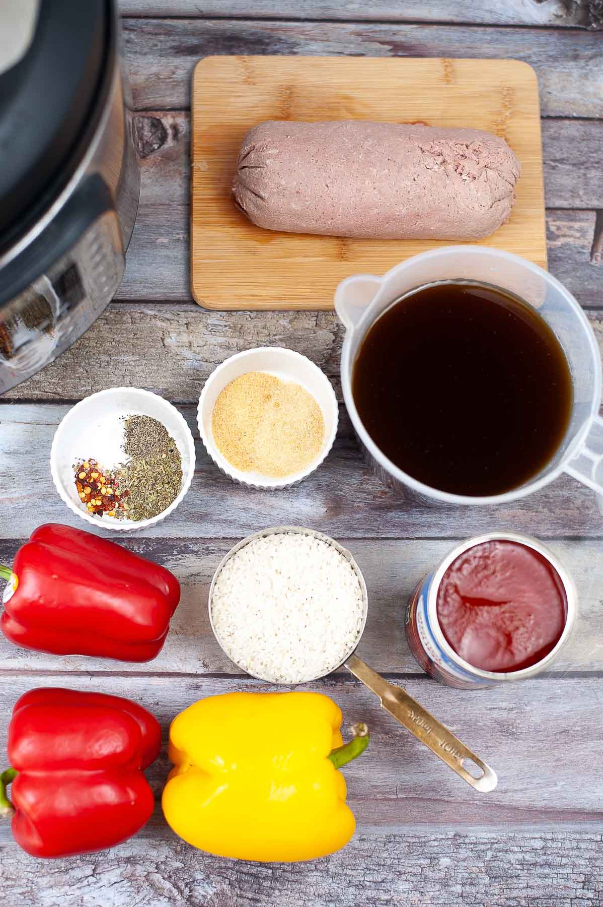 ingredients for stuffed pepper soup on a wood table - red and yellow bell pepper, cup of white rice, ground turkey, beef broth, tomato sauce and spices