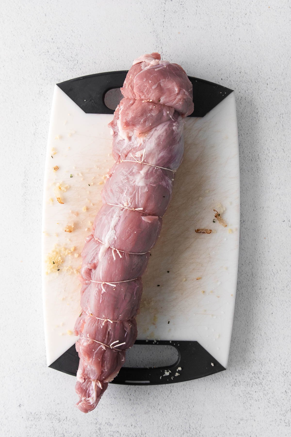 raw pork tenderloin tied with twine on a white cutting board