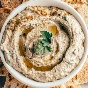 closeup of a white bowl of baba ganoush eggplant dip topped with olive oil and sprigs of fresh parsley