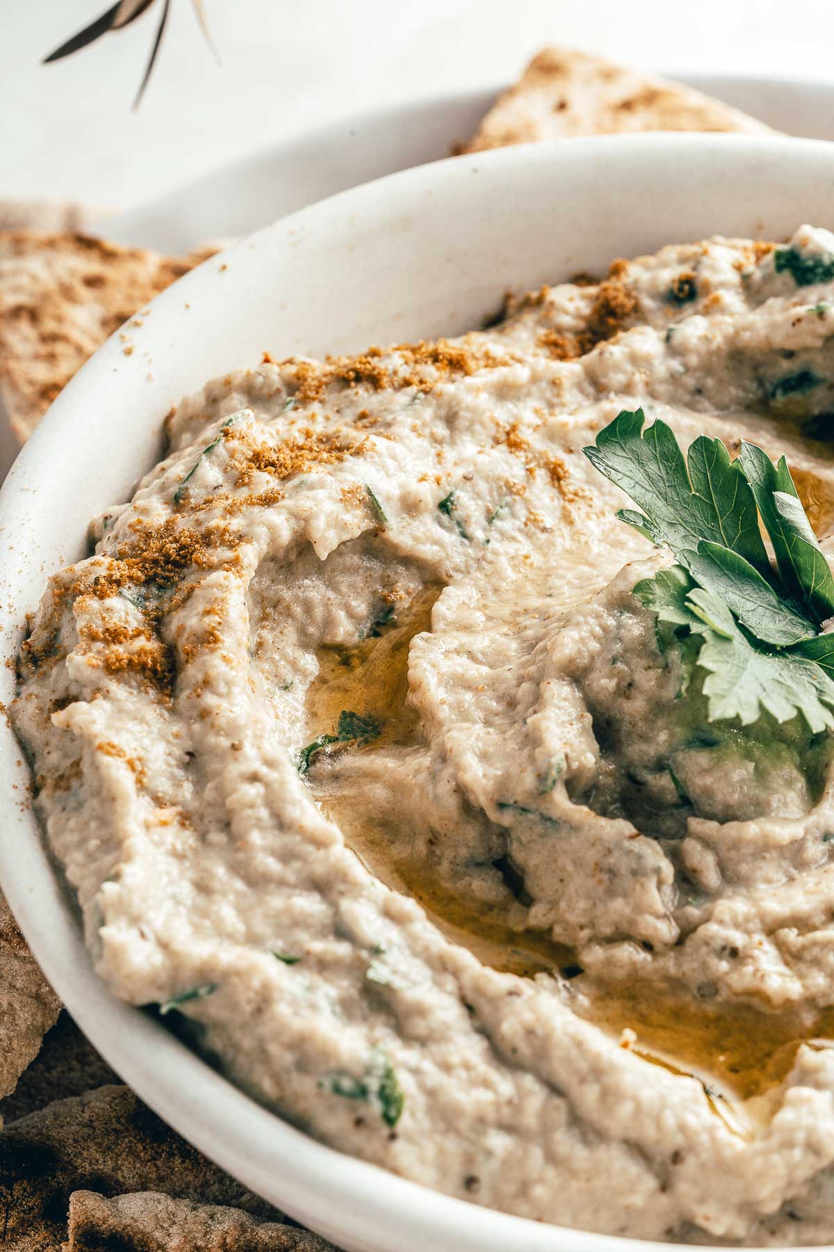 closeup of a white bowl full of eggplant dip drizzled with olive oil and topped with parsley