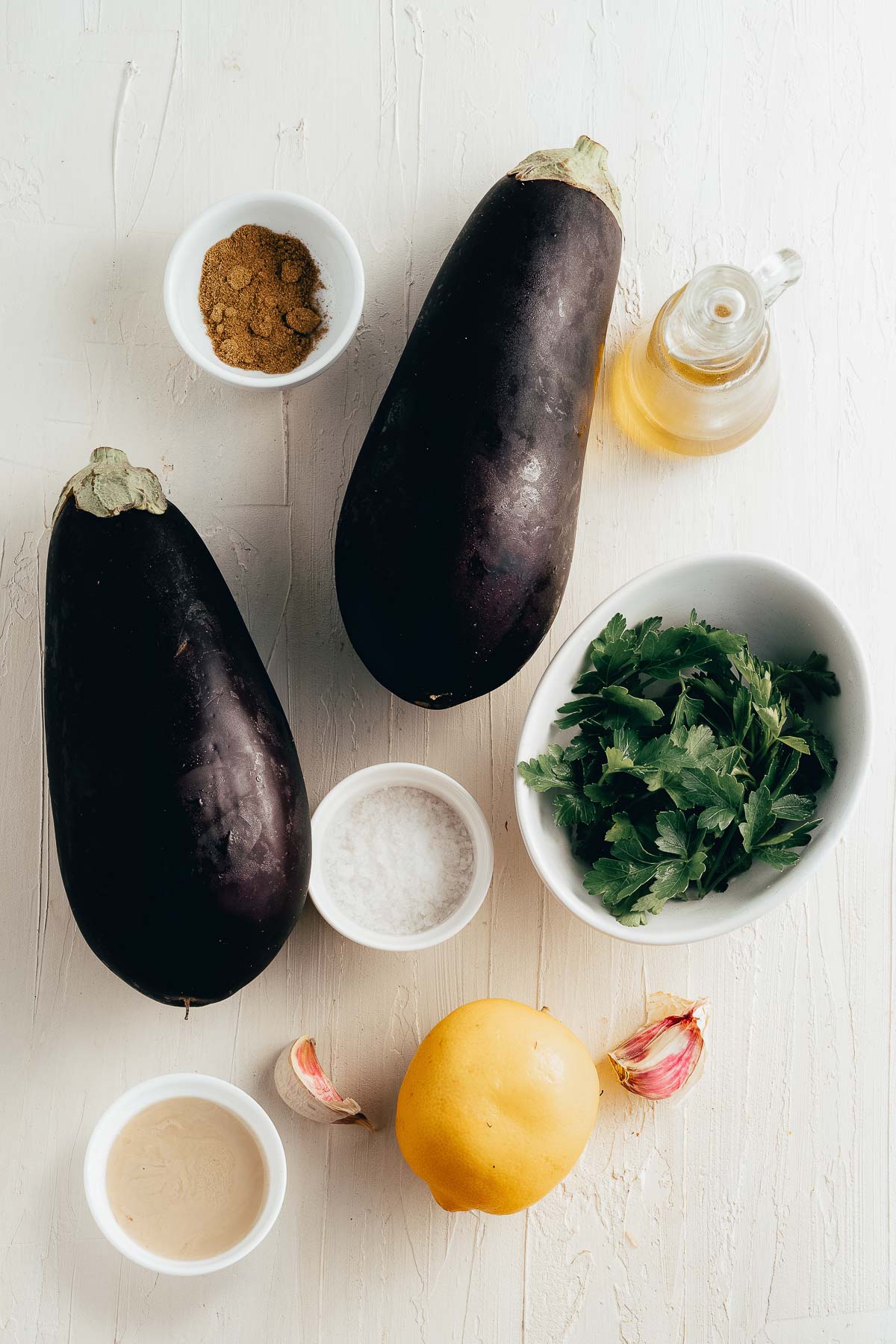 two large eggplant, lemon, and small white bowls of lemon juice, spices, olive oil, salt and parsley