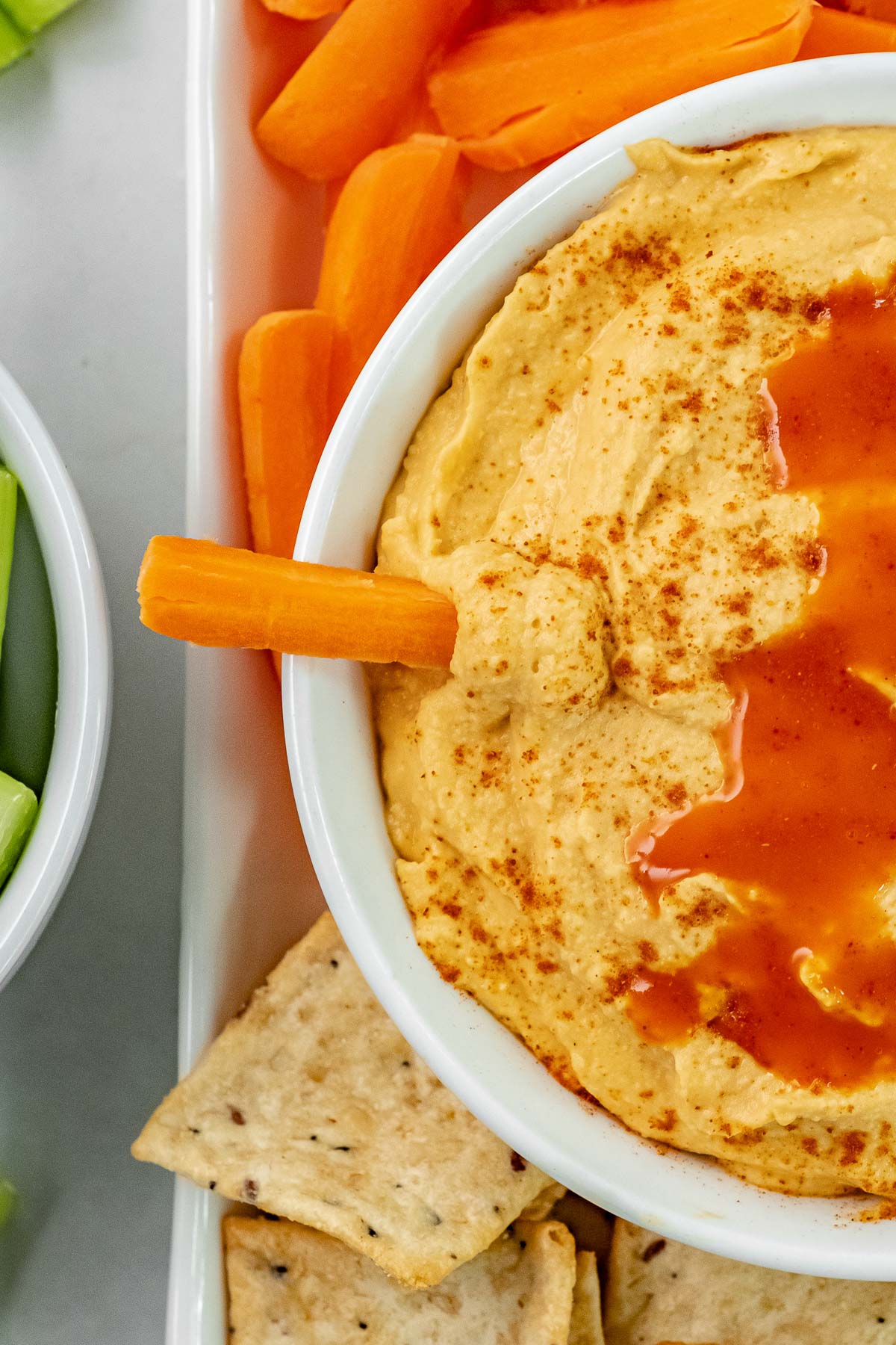 white bowl with buffalo hummus with a carrot slice dipped in
