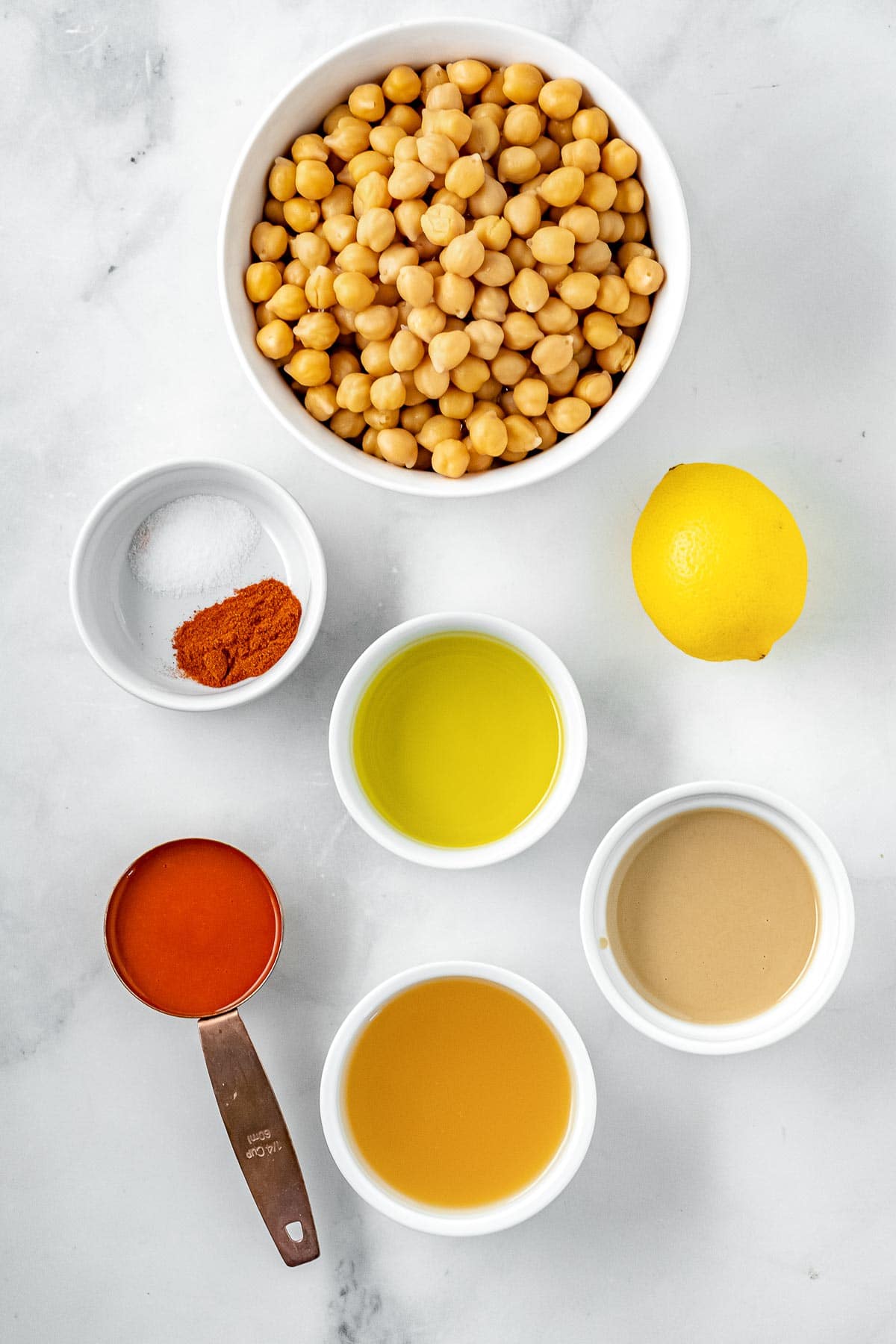 several white bowls full of ingredients for hummus - chickpeas, lemon, buffalo sauce, chickpea liquid, olive oil and spices