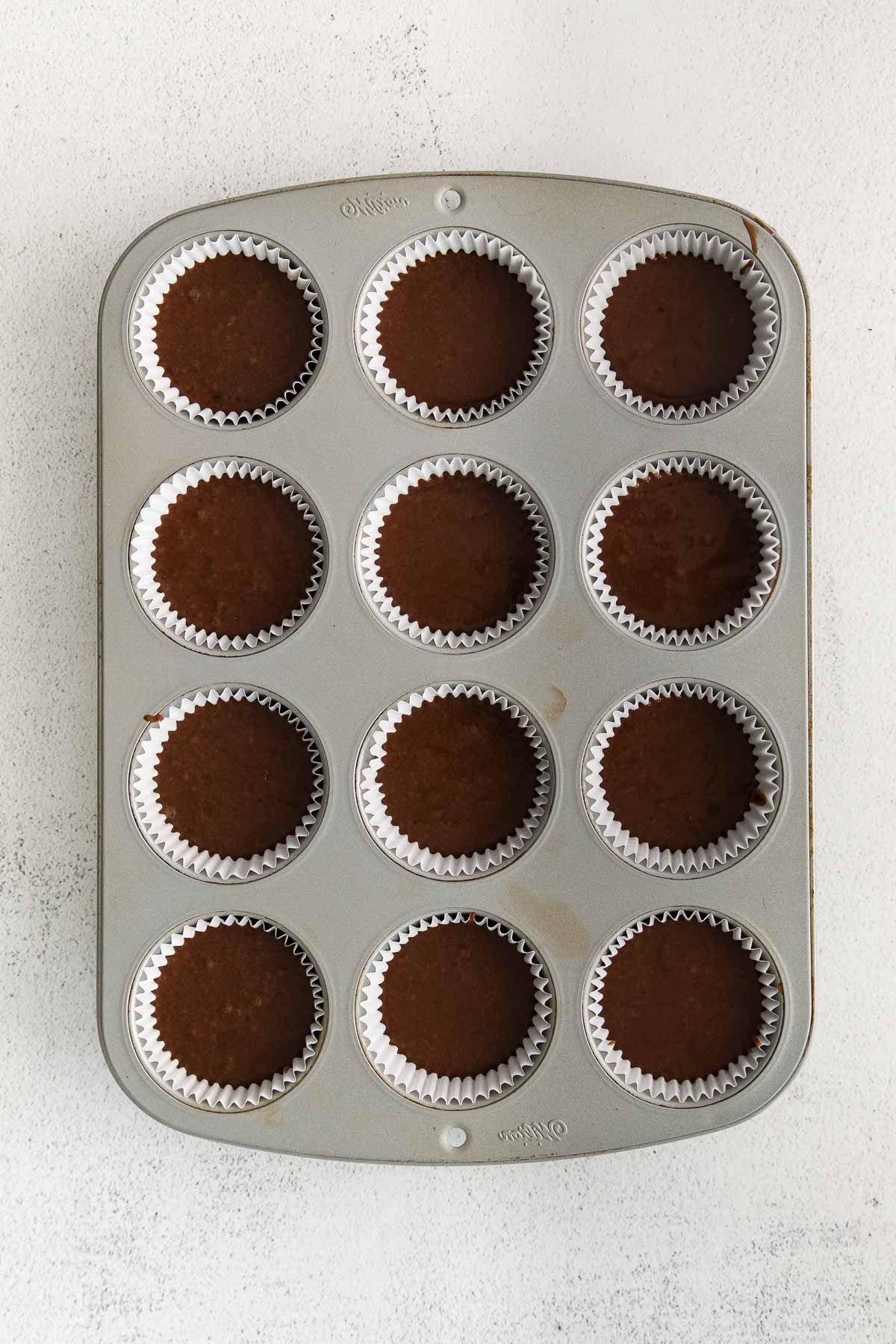 muffin tin with chocolate batter in white paper liners