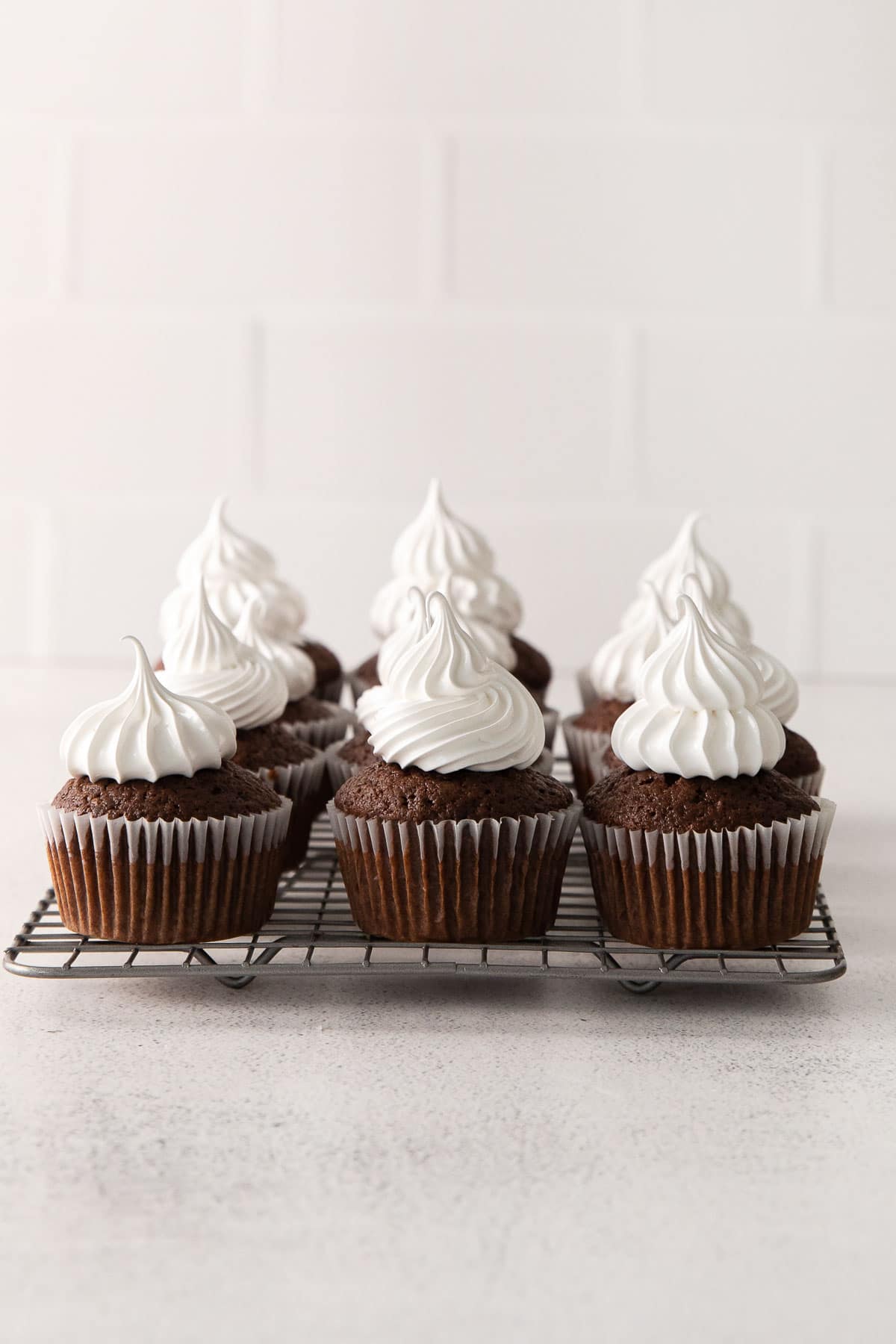 several chocolate cupcakes topped with white marshmallow frosting on a white rack