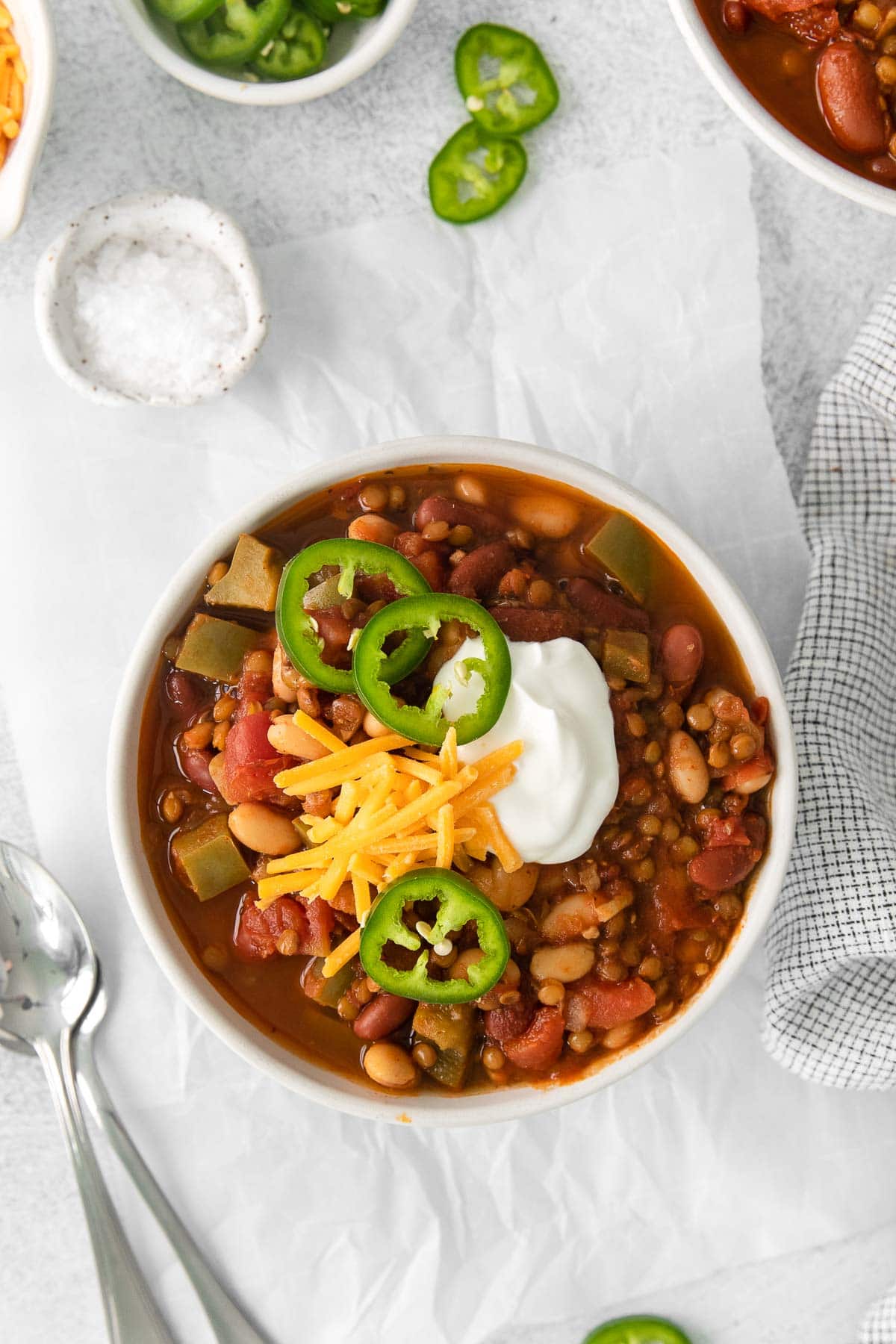 white bowl full of lentil chili topped with shredded cheese, sour cream and sliced jalapenos