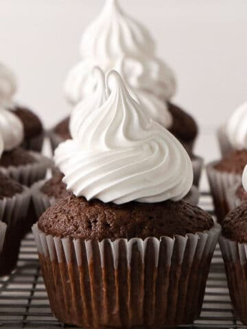 closeup of a wire rack with several chocolate cupcakes topped with white marshmallow frosting