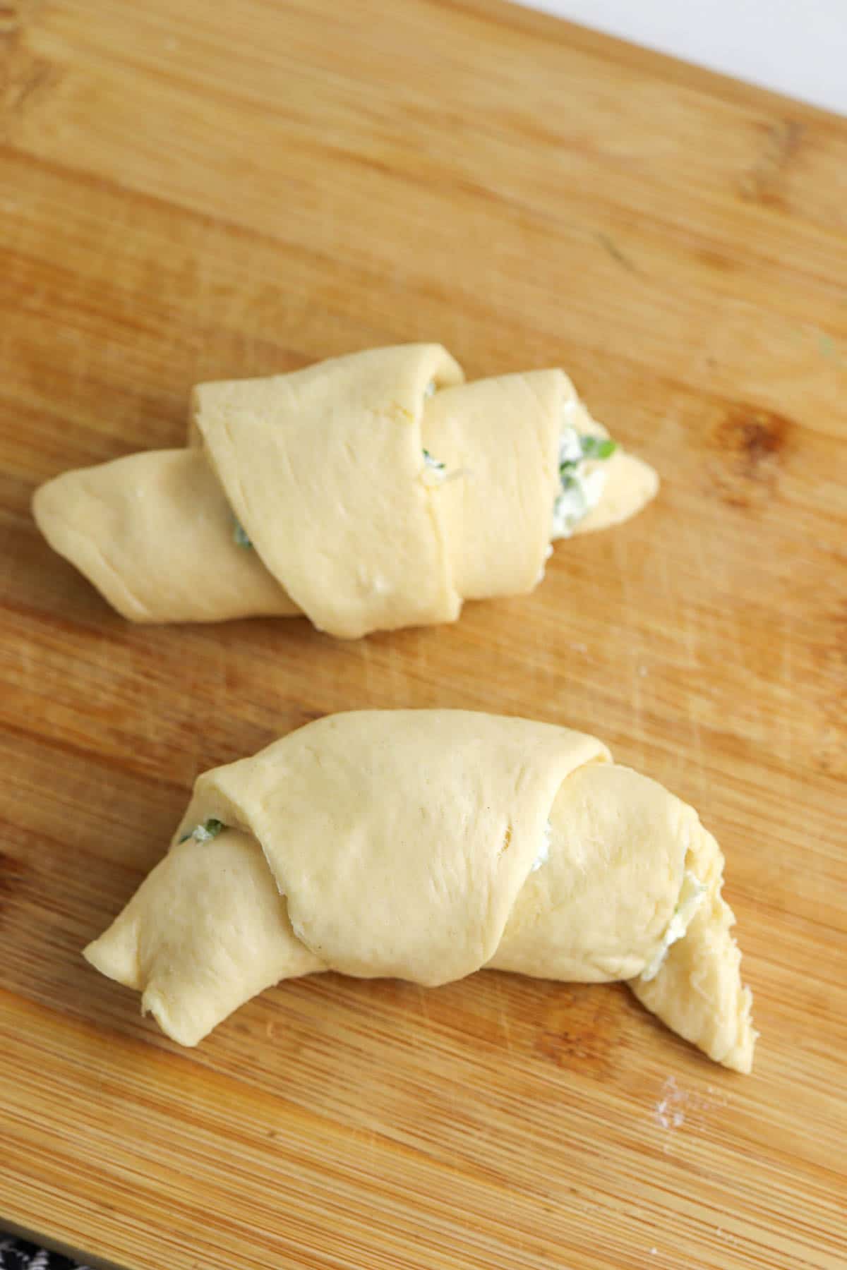 two rolled up crescent roll dough on a wood cutting board