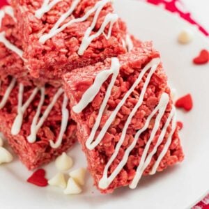closeup of a red rice krispie treat with white drizzle on a plate with valentine's day candy and white chocolate chips