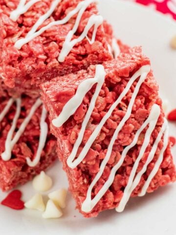 closeup of a red rice krispie treat with white drizzle on a plate with valentine's day candy and white chocolate chips