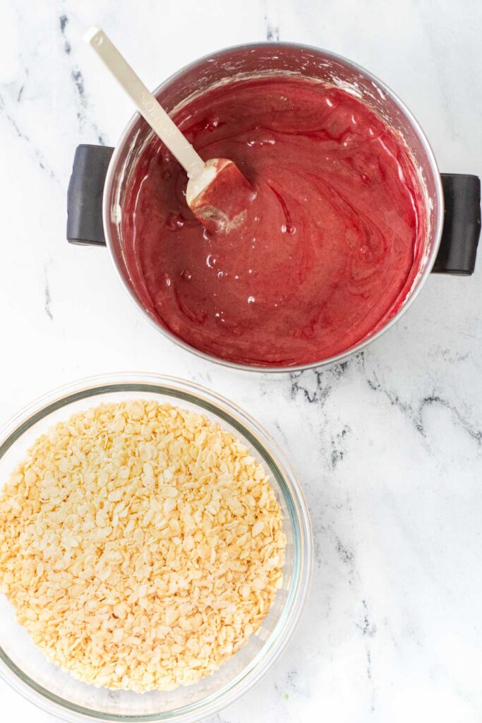 big pot of red velvet marshmallow mixture and a big glass bowl of rice krispie cereal