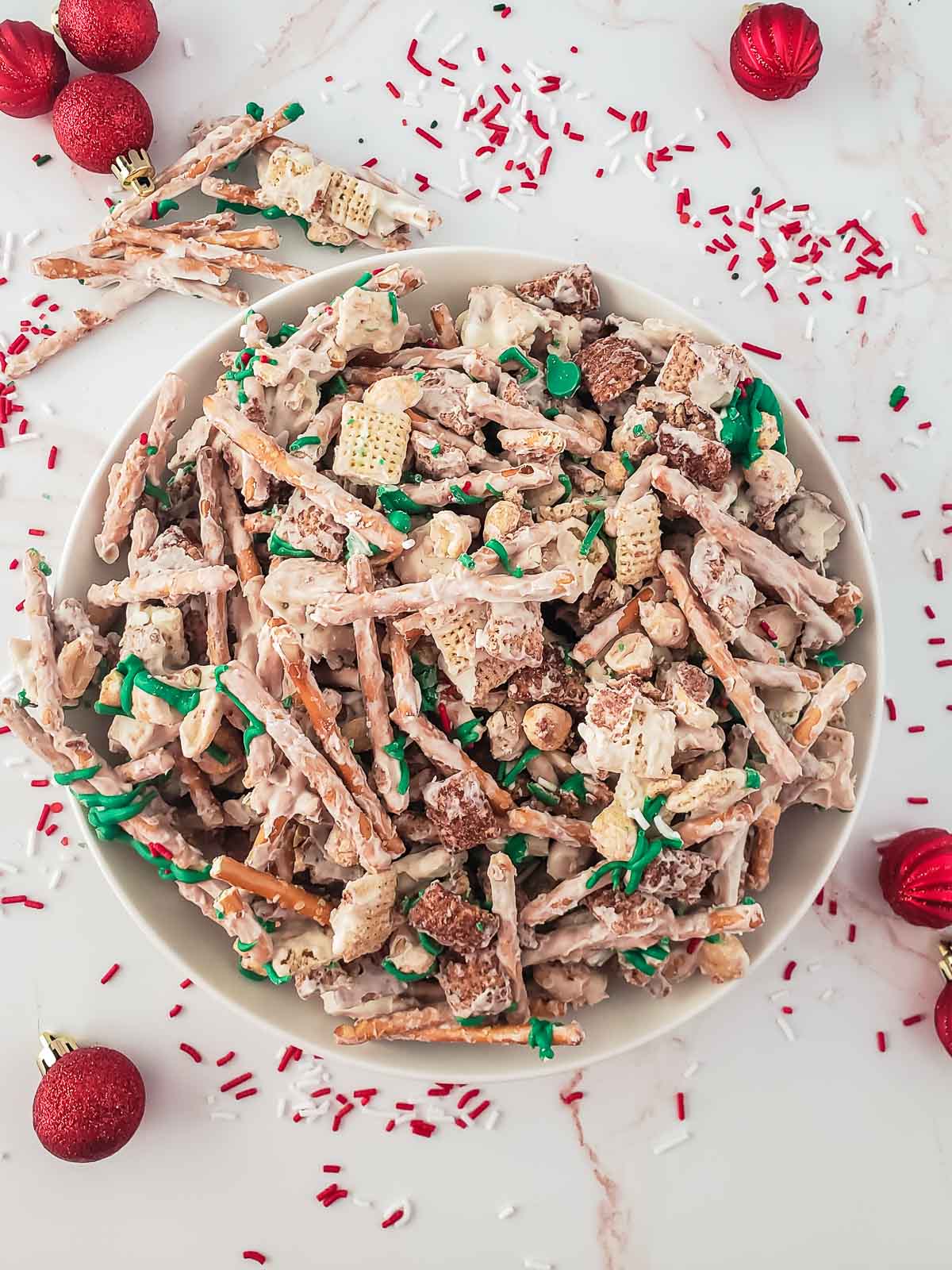 white bowl full of white chocolate chex mix with pretzel sticks and peanuts and green and red sprinkles
