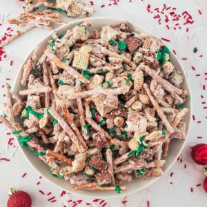 white bowl full of white chocolate chex mix with pretzel sticks and peanuts and green and red sprinkles