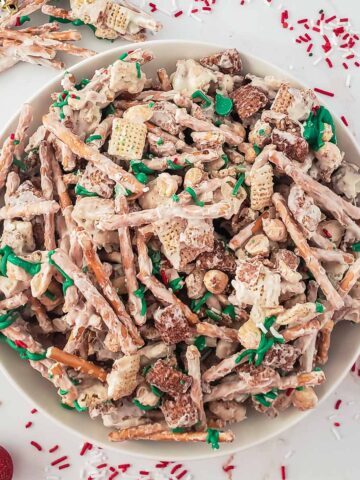 white bowl full of white chocolate chex mix with pretzel sticks and peanuts and green and red sprinkles