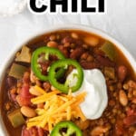white bowl full of chili with sliced jalapenos, shredded cheese and sour cream