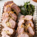 stuffed pork tenderloin sliced in several pieces on a white serving platter