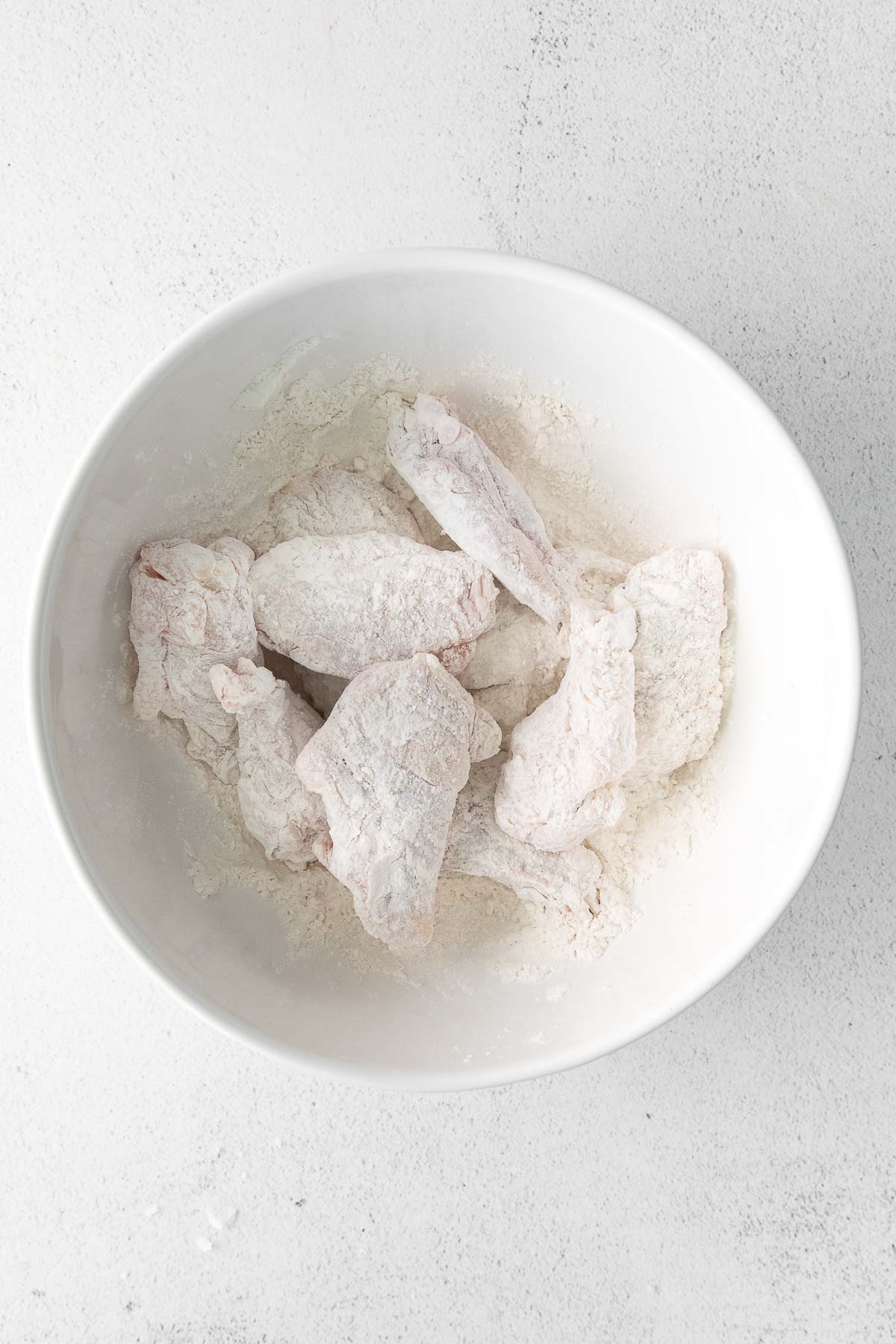 white bowl with several raw chicken wings tossed in flour mixture