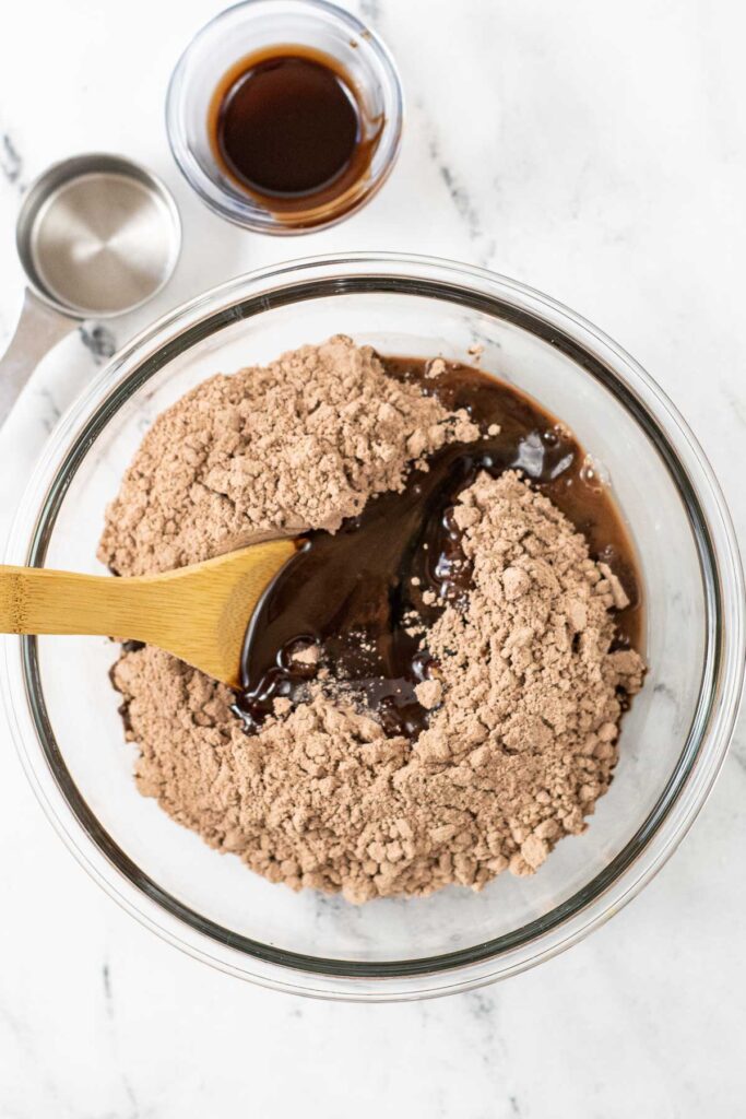 brownie mix in a glass mixing bowl with chocolate syrup poured in