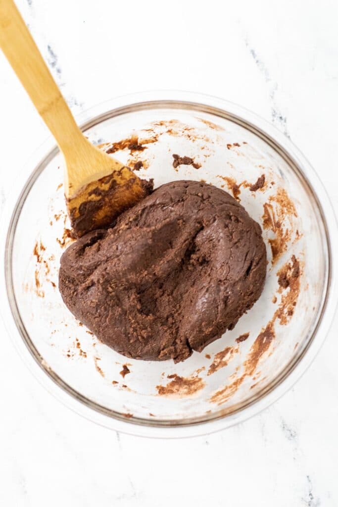 thick brownie batter in a big glass bowl with a wooded spoon