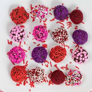 several sprinkle covered brownie truffles on a white plate