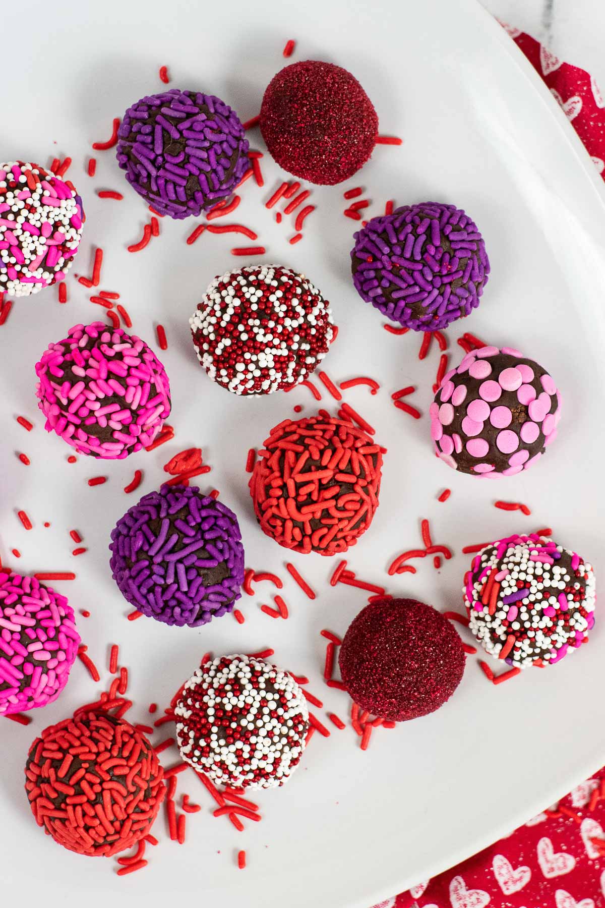 white plate with 14 brownie truffle balls covered in different colored sprinkles - red, purple, red, white 