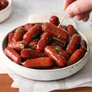 a white bowl full of little smokies cocktail weiners with a toothpick picking one up
