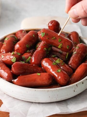 a white bowl full of little smokies cocktail weiners with a toothpick picking one up
