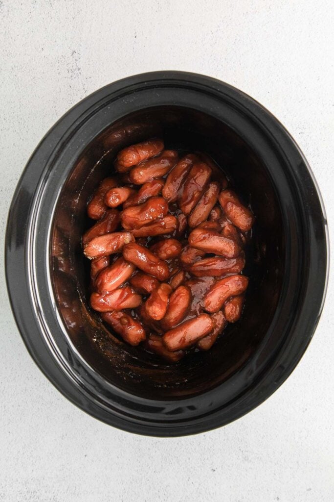 black slow cooker with little smokies hot dogs in a sauce