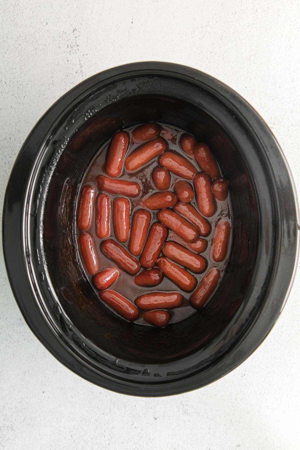 little smokies cocktail sausages cooking in a bbq sauce in a black crock pot