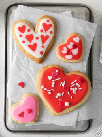 four heart shaped shortbread cookies with pink and red icing with sprinkles