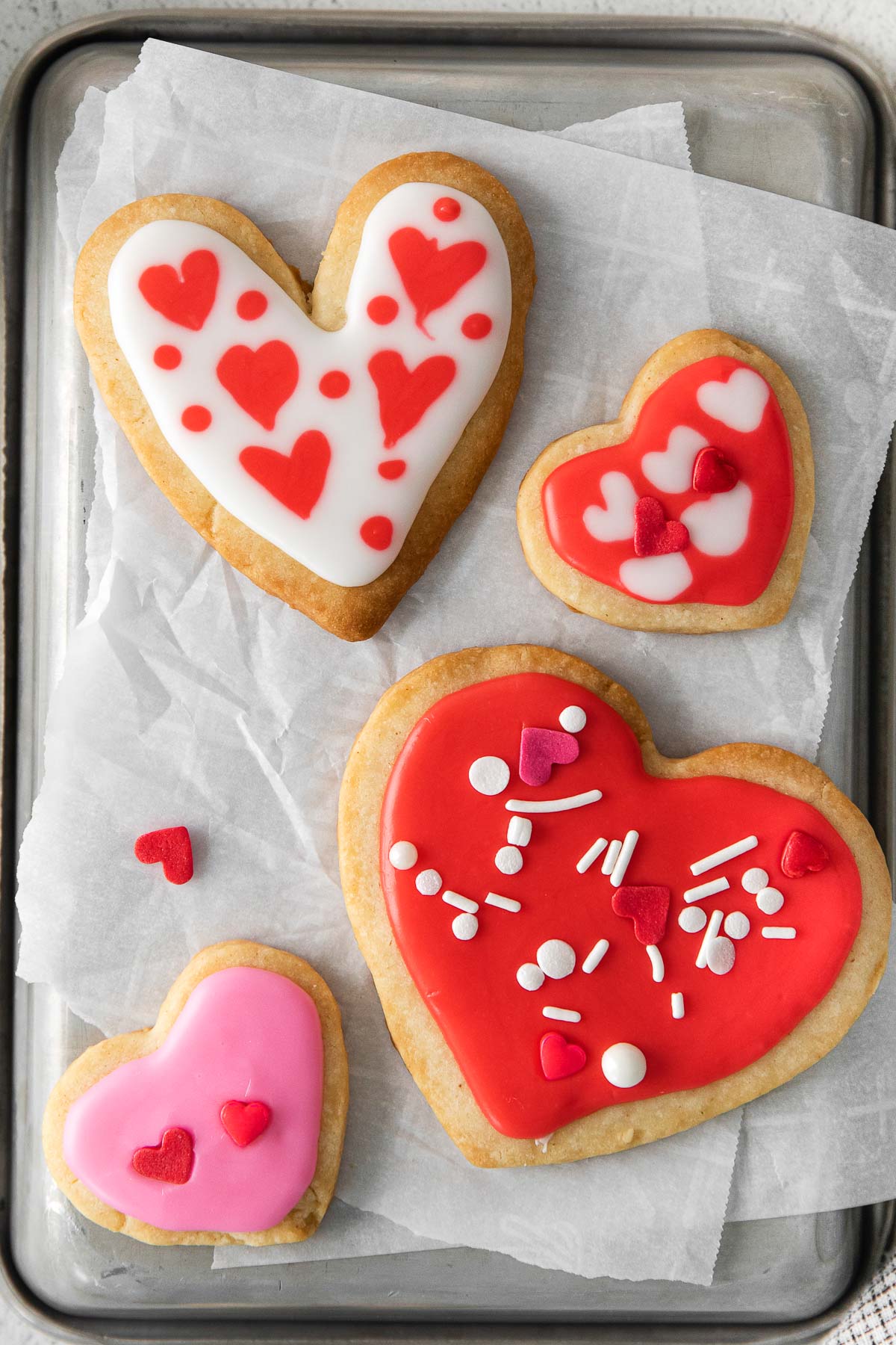 closeup of four pink and red iced shortbread cookies with valentine themed sprinkles
