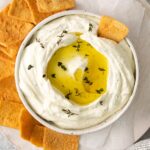 closeup of a white bowl full whipped feta dip topped with olive oil and fresh herbs