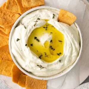 closeup of a white bowl full whipped feta dip topped with olive oil and fresh herbs