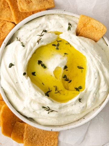closeup of a white bowl full whipped feta dip topped with olive oil and fresh herbs