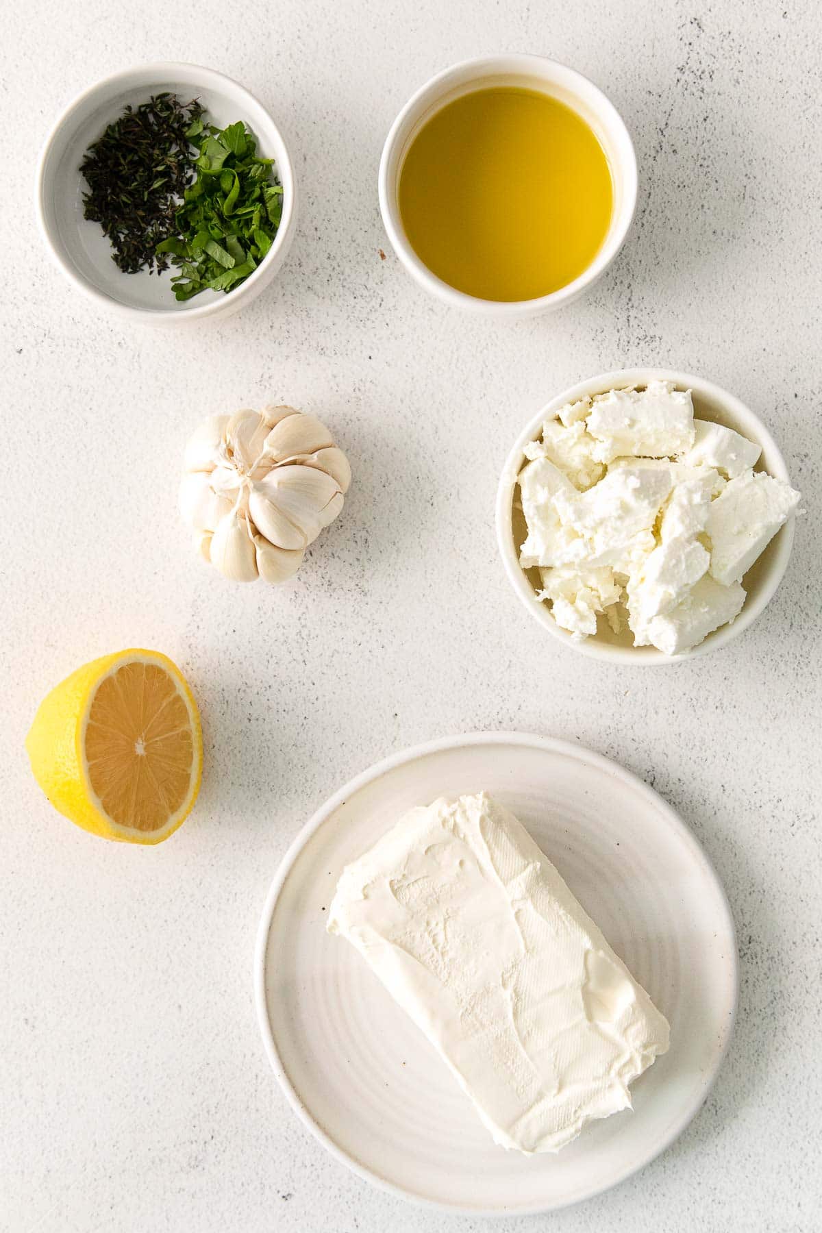 several white bowls with ingredients for feta dip - feta cheese, block of cream cheese, thyme, olive oil and lemon