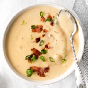 closeup of bowl of creamy cheese soup with bacon on top and a silver spoon full