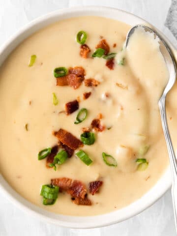 closeup of bowl of creamy cheese soup with bacon on top and a silver spoon full