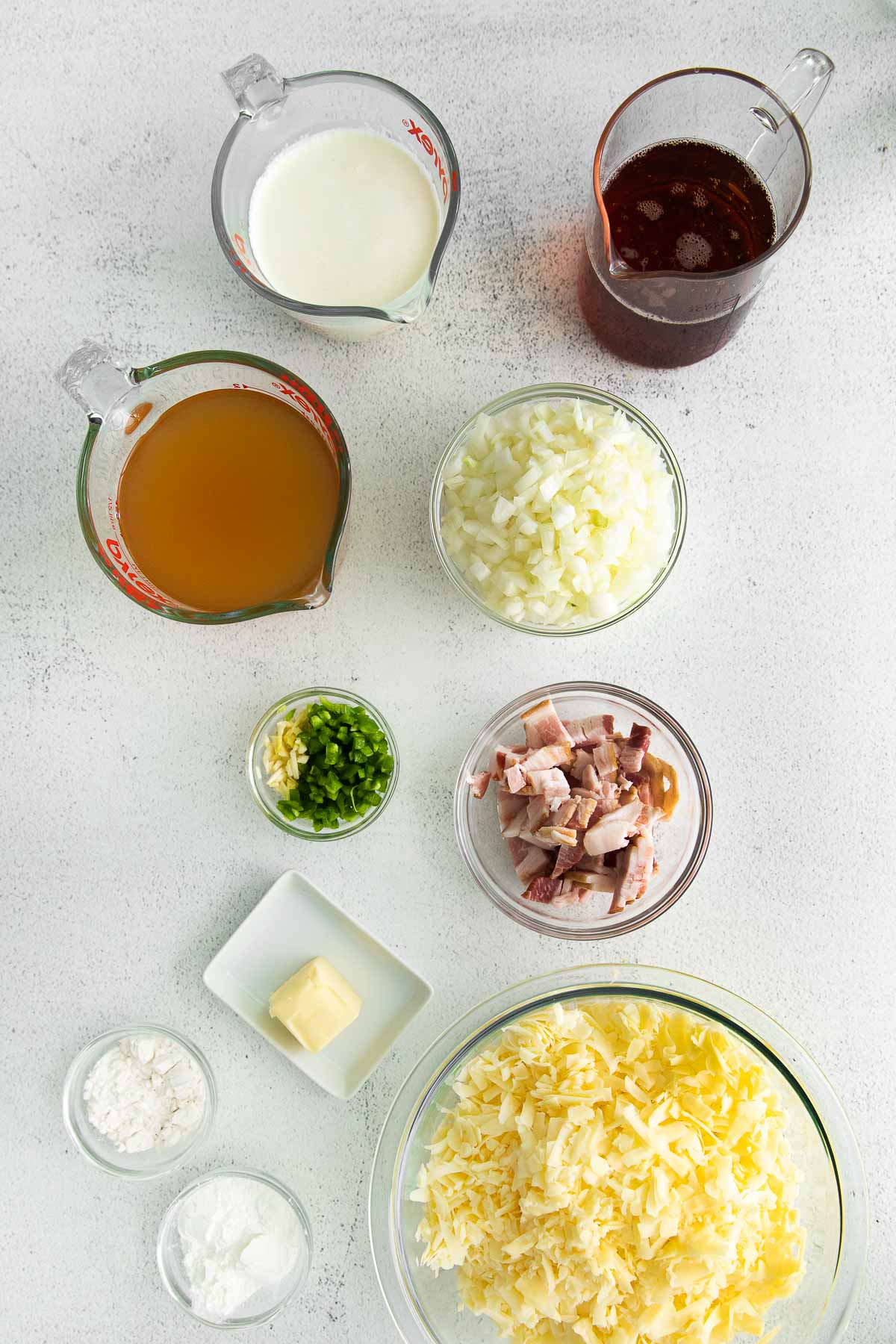 several glass bowls of ingredients for beer cheese soup - shredded cheddar cheese, bacon, butter, broth, diced onions, cornstarch