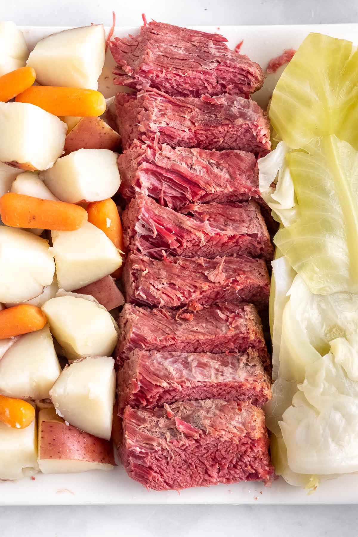 platter with rows of sliced corned beef, cut potatoes, baby carrots and cabbage