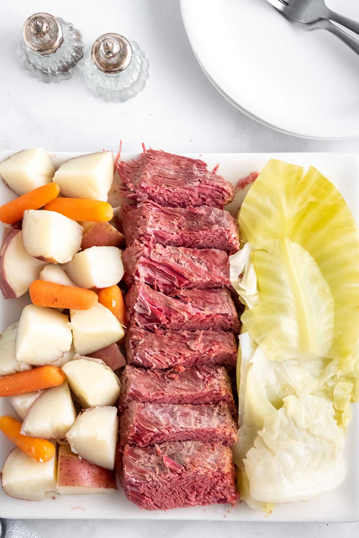 white platter with sliced corned beef, diced potatoes and baby carrots and cooked cabbage