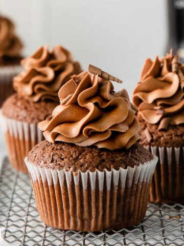 three chocolate cupcakes in white liners topped with chocolate frosting