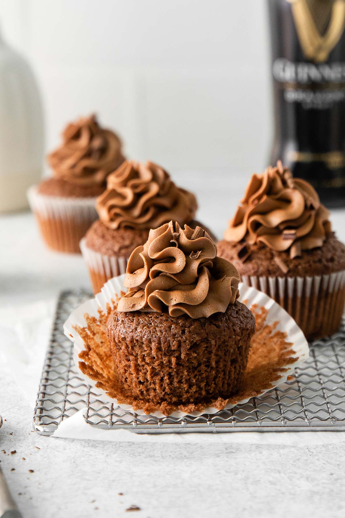 three guinness chocolate cupcakes with chocolate frosting on a wire rack with the white liner pulled back