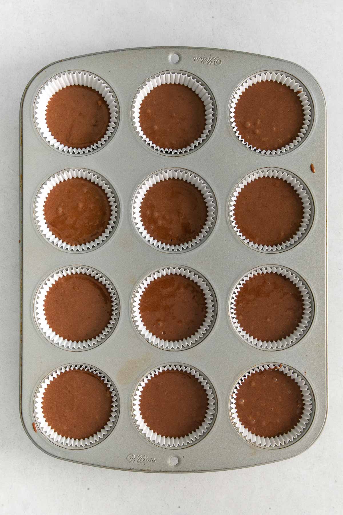 muffins tin with chocolate cupcake batter in white paper cups