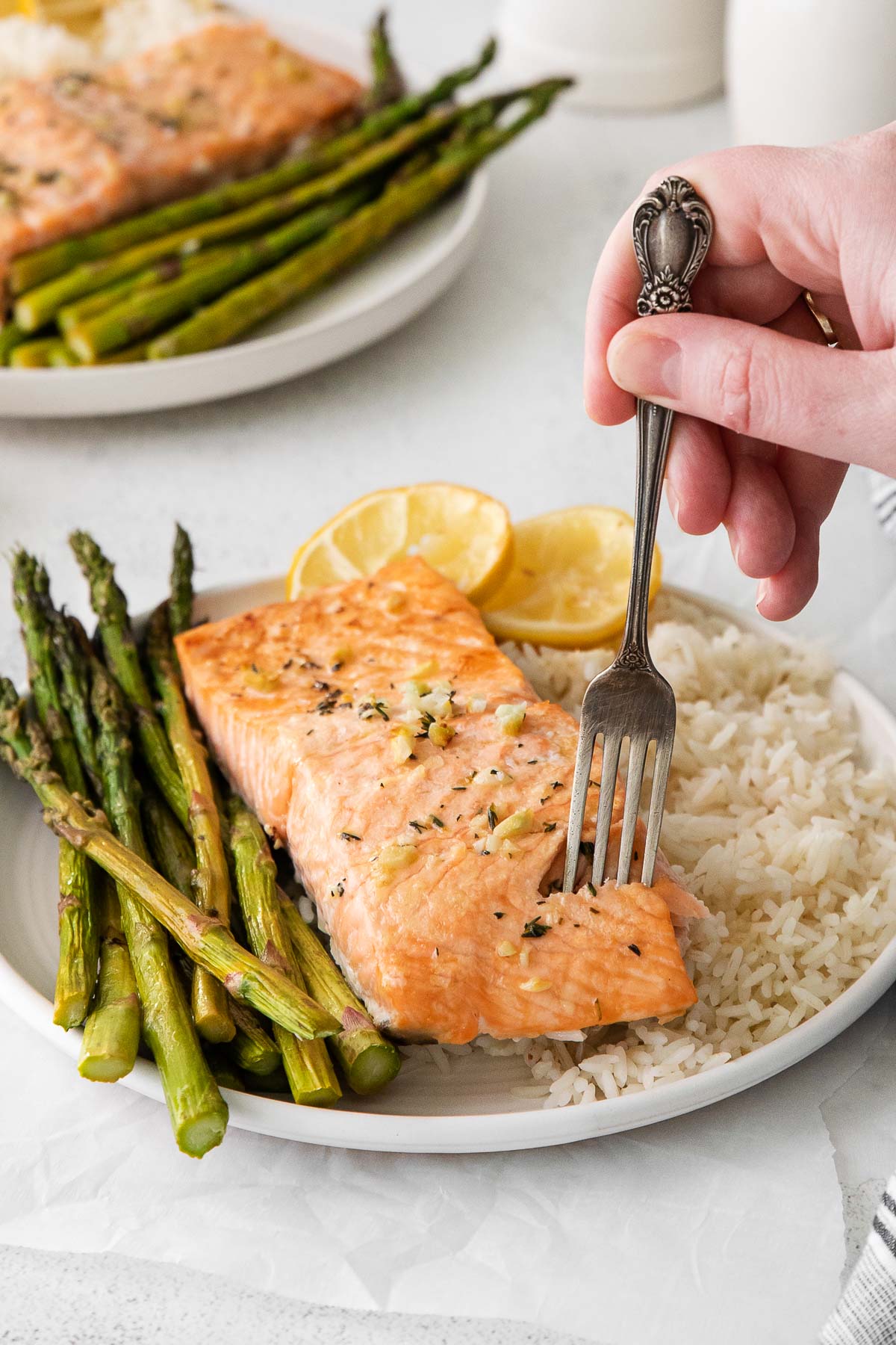 baked salmon fillet with a fork in it on a plate with asparagus and rice