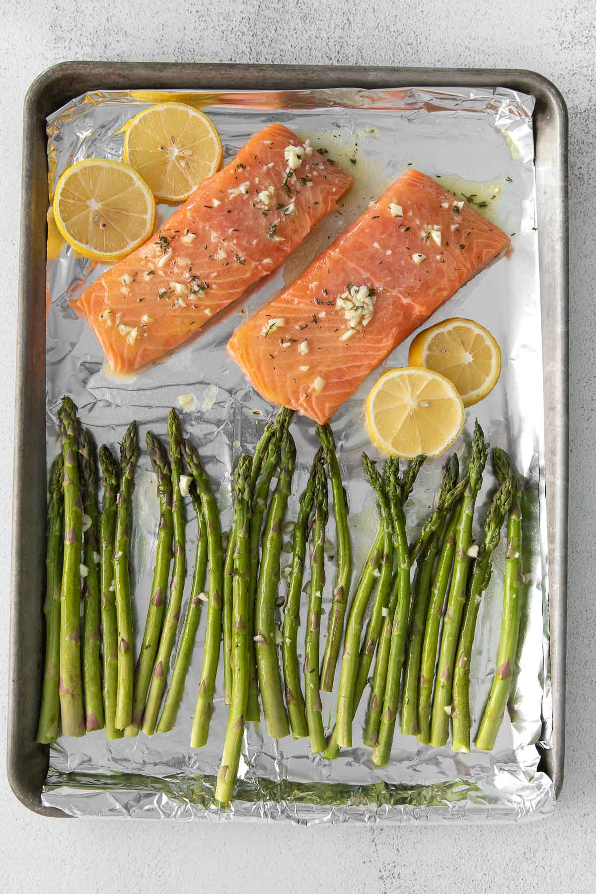 sheet pan with raw salmon and raw asparagus and lemon slices