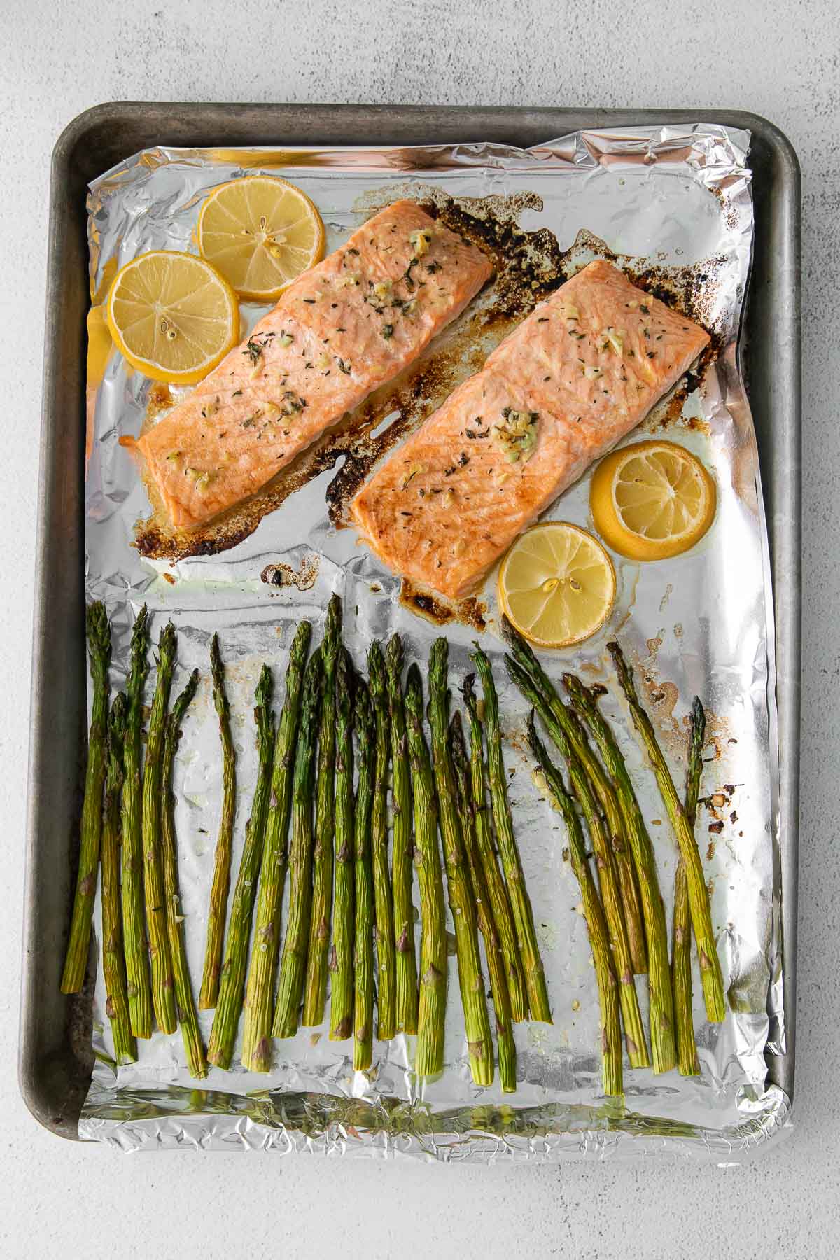 baking sheet with two baked salmon and several asparagus spears and lemon slices