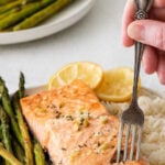 white plate with baked salmon fillet with a fork inserted in and alongside asparagus and rice